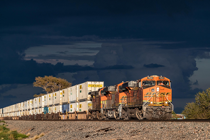 A BNSF double-stack intermodal train hauls containers in New Mexico with a rainstorm on the horizon.